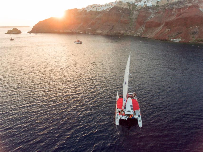 Santorini: Cruise Catamaran with BBQ & Drinks Day or Sunset - Sailing Below the Cliffs Toward Oia Sunset